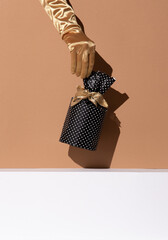 Hand in golden gloves holding gift box. Minimal still life design. Holiday,christmas, concept