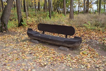 Bench similar to a small boat made of a tree trunk is installed in the park among the autumn trees © Anatolijs