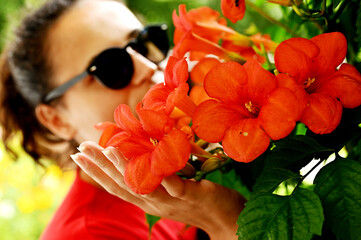 Beautiful young woman smelling red flowers in the park.