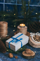 Christmas white gift box with blue bow ribbon, wooden decorations, candle, nuts on magic dark blue background. Vintage Xmas greeting card mockup, postcard.