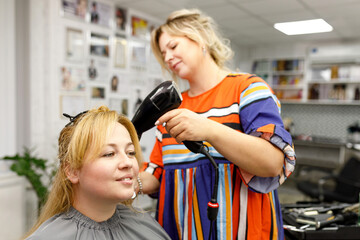 Young woman in a hairdressing salon. Hairdresser dries customer's hair. Focus on client