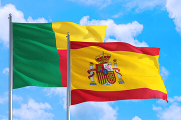 Spain and Benin national flag waving in the windy deep blue sky. Diplomacy and international relations concept.