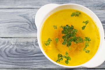 Chicken soup with herbs, in a white plate, on a wooden background