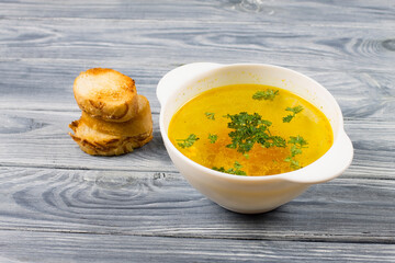 Chicken soup in a white plate with bread, on a wooden background