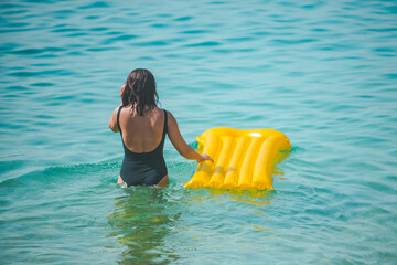 woman with yellow inflatable mattress walking to sea