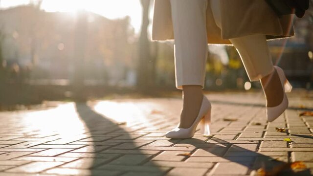 Unrecognizable Beautiful Business Woman Legs in high heels walks through city park to work in the office in autumn in sunset light. Close-up. Slow motion.