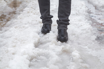 Young adult man legs in black leather boots walking on wet melting snow in winter day. Front view....