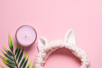 Funny hair band, aromatic candle and palm leaf on pink pastel background. Home spa concept.