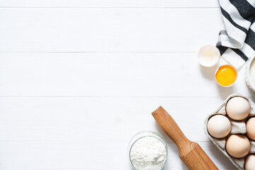 Baking ingredients: flour, eggs, sugar with a rolling pin on a light white wood background. With copy space.