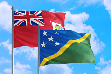 Solomon Islands and Bermuda national flag waving in the windy deep blue sky. Diplomacy and...