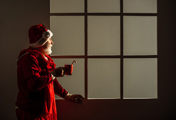 Naklejka premium man in santa hat drink milk or cocoa with stick. The morning before Xmas. enjoy the winter holiday. delivery new year gifts. Christmas online shopping. santa claus with white beard