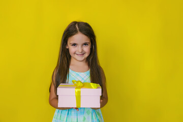 The child has a happy face holding a gift box on a yellow background. The kid is happy, loves birthday and holidays.