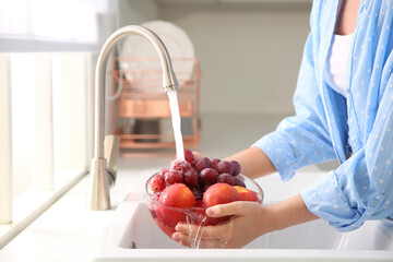 Woman washing fresh grapes and nectarines in kitchen sink, closeup