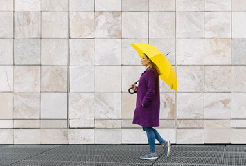 Woman walking with a yellow umbrella on a stone architecture background © Juan Rodríguez