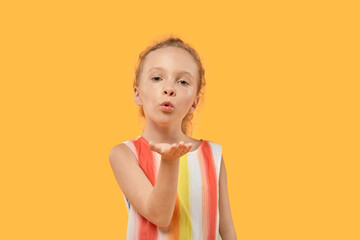 Cute little blonde girl blows a kiss. Bright dress. Orange background.