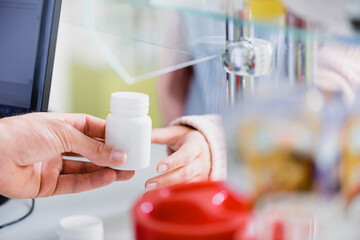 cropped view of pharmacist giving bottle with medication to customer near computer monitor