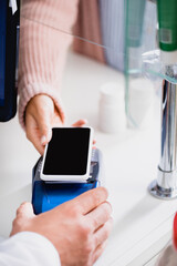 cropped view of woman paying with smartphone in drugstore