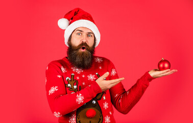 happy caucasian guy await new year present. lets have fun. Santa Claus hipster. man at Christmas. brutal bearded male red background. party man with Christmas tree decorative ball. copy space