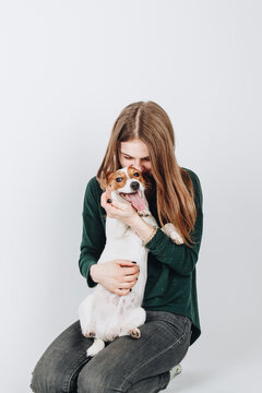 Cute young woman kisses and hugs her puppy jack russell terrier dog. Love between owner and dog. Isolated on white background. Studio portrait.