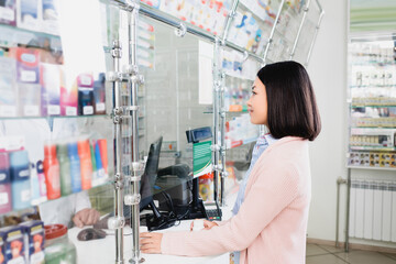 side view of asian customer holding bottles with pills near seller in drugstore