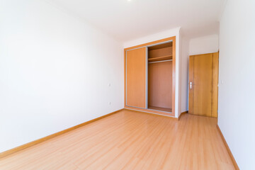 Empty room with dark wooden floating laminate flooring and wardrobe. House interior, wide bedroom space. Newly recently painted new apartment or house. Wood floor. Real state and property management