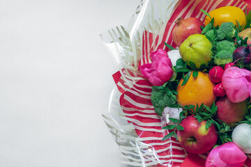 The arrangement of fruit, vegetables, flowers and green leaves surrounded by ornate red and white translucent striped paper on a white background with copy space. Closeup, view from above