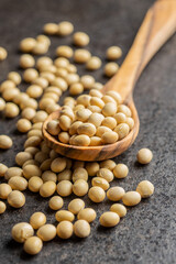 Dried soy beans in wooden spoon on black table.
