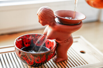 Chinese tea figure, a sieve of red clay. Girl with naked breasts and hands behind his back. Tea is poured from above into a sieve and poured from the nipples into a bowl. Close-up, blurred background.