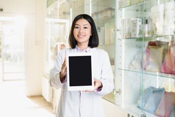 cheerful asian pharmacist in white coat holding digital tablet with blank screen in drugstore