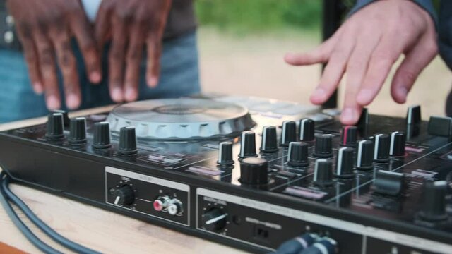 Sequence of shots of male caucasian dj adjusting sound and mixing music on dj deck playing remixes at summer open-air party in front of cheerful audience
