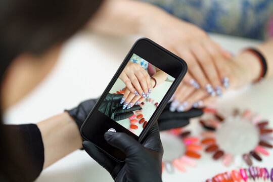 Manicurist takes a photograph of her work, beautiful woman manicure, with a smartphone