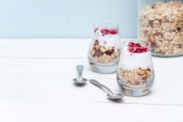 Homemade yougurt with granola and pomegranate fruit in glasses on white wooden table. Healthy breakfast.