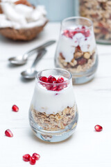 Homemade yougurt with granola and pomegranate fruit in glasses on white wooden table. Healthy breakfast.