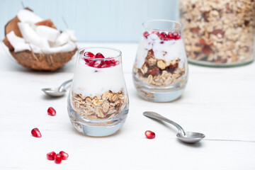 Homemade yougurt with granola and pomegranate fruit in glasses on white wooden table. Healthy breakfast.