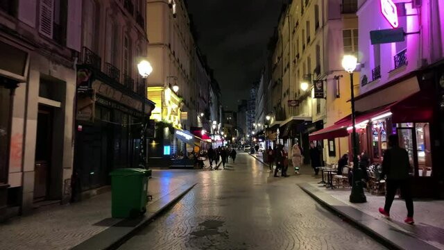 Time lapse night footage of people walking on famous street called "Rue Montorgueil". It is lined with restaurants, cafes and bakeries. Lens effects occur.