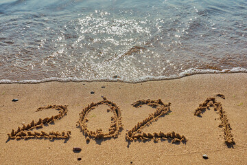 Year 2021 inscription on a tropical sandy beach with waves and foam on a background.