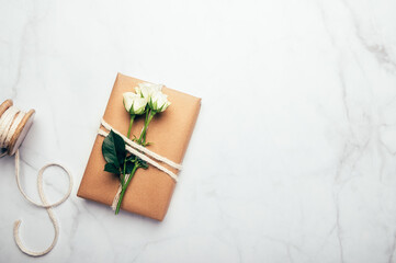 Gift wrapped in recycled brown paper decorated with real fresh roses, on light background with minimalist style wrapping, top view flat lay, eco friendly and zero waste packaging