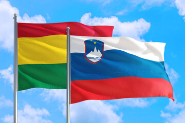Slovenia and Bolivia national flag waving in the windy deep blue sky. Diplomacy and international relations concept.