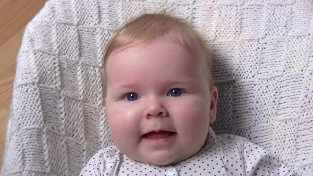 A little adorable blue-eyed baby on a white blanket is looking at the camera