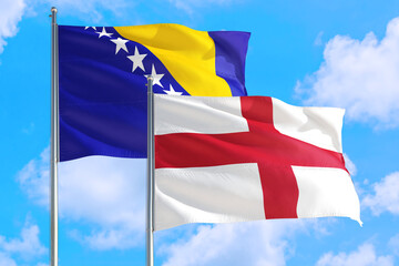 England and Bosnia Herzegovina national flag waving in the windy deep blue sky. Diplomacy and international relations concept.
