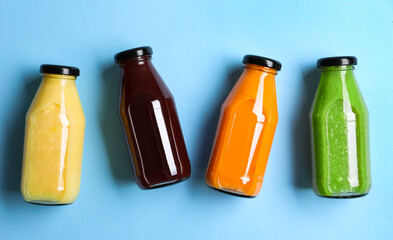 Bottles with delicious colorful juices on light blue background, flat lay