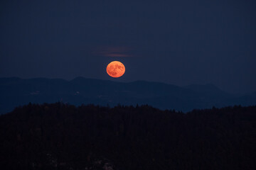 huge orange full moon rising behind a mountain ridge with layers of hills in the foreground...