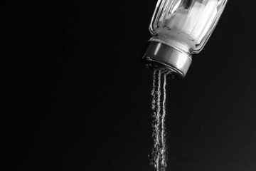 Pouring salt from shaker on black background, closeup. Space for text