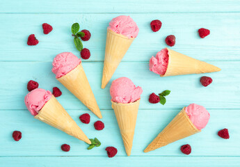 Flat lay composition with delicious pink ice cream in wafer cones and raspberries on light blue wooden table, flat lay