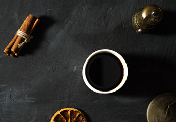 A cup of coffee with cinnamon an orange on the black background