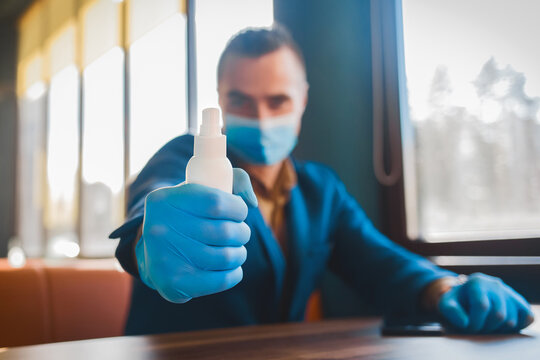 Young caucasian guy businessman in a suit with protective gloves and a medical mask holding a hand sanitizer