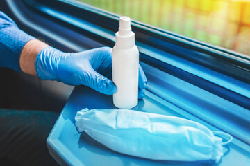 A man's hand in a medical glove takes an antiseptic next to a protective white mask, soft focus
