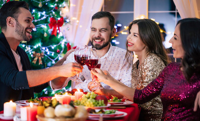 Group of happy excited beautiful friends while they are eating with glasses wine in hands at a home christmas party and having fun.