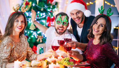 Group of happy excited beautiful friends while they are eating with glasses wine in hands at a home christmas party and having fun.