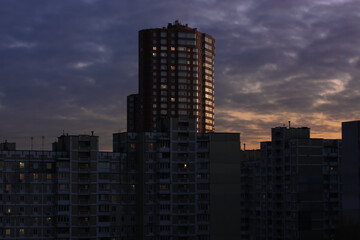Obraz premium Tall red brick building and many other houses behind it against the background of a purple orange pre-sundown sky in the evening. Modern architecture Kiev, Ukraine